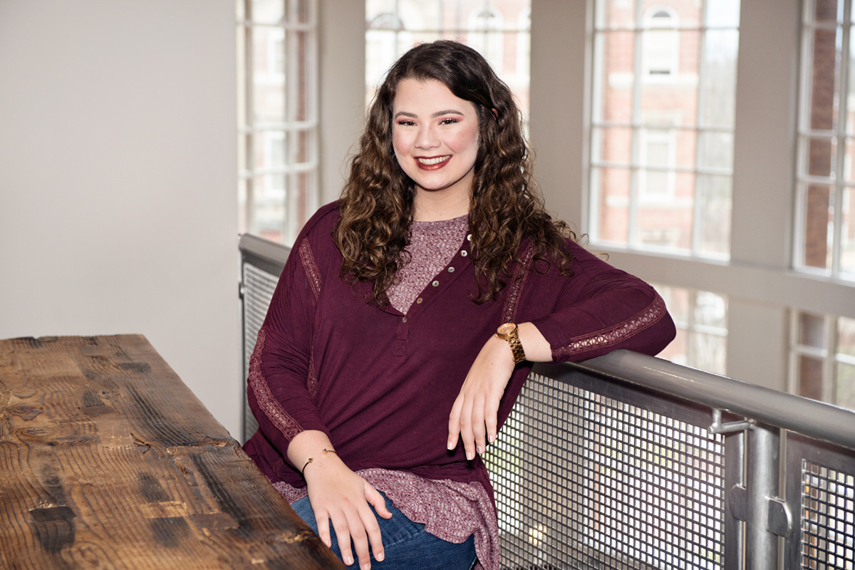 Shelby Baldwin, pictured at a wooden table at McCool Hall.