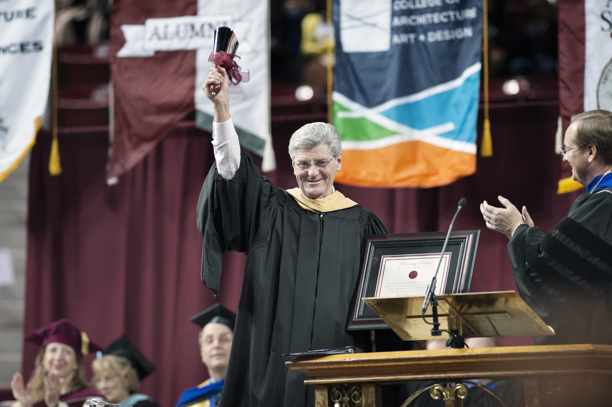 Gov. Phil Bryant rings a cowbell during Mississippi State University fall commencement ceremonies after MSU President Mark E. Keenum, right, presented him with the bell and a certificate declaring the governor an "Honorary Bulldog." The university conferred degrees upon nearly 1,400 graduates.