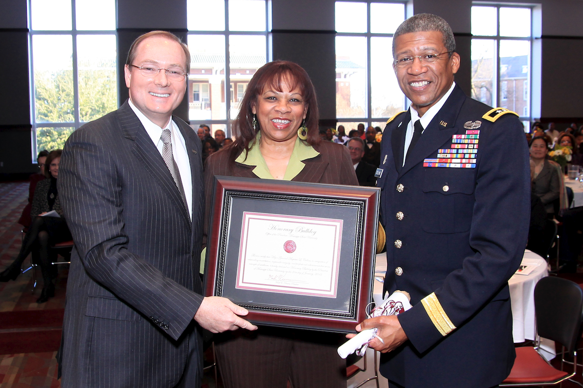 Mississippi State University President Mark E. Keenum. left, confers "Honorary Bulldog" status on Mississippi Adjutant Gen. Augustus L. Collins, right, speaker for MSU's annual community Martin Luther King Jr. Day Unity breakfast held Monday in the Colvard Student Union. Shown at center is the general's wife, Mrs. Debra Collins. Hundreds attended the event, which featured a celebration of King's life and work. Collins is the first African-American to lead the Mississippi Army and Air National Guard.