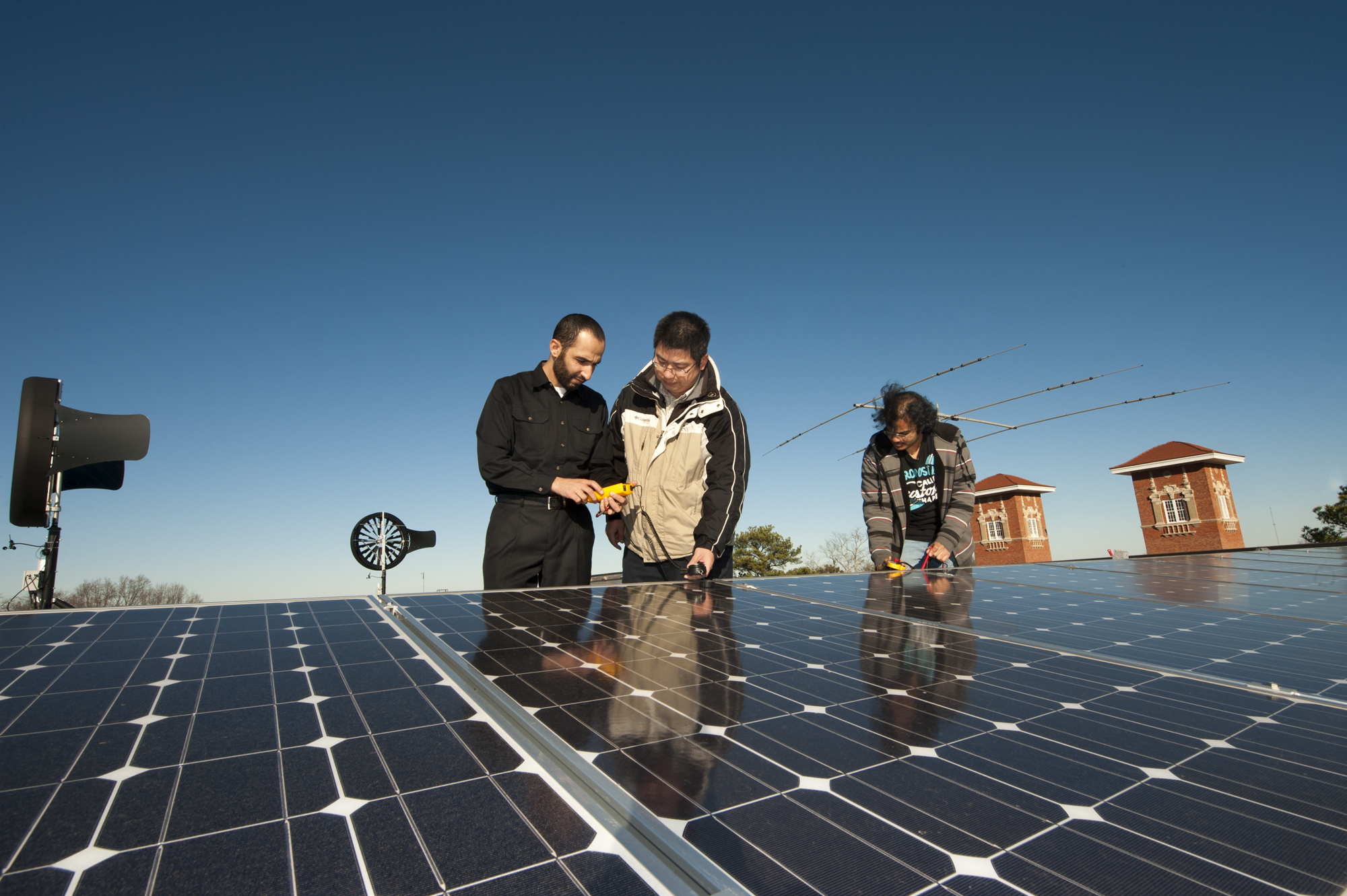 Mississippi State University's Simrall Electrical & Computer Engineering Building features an energy farm with solar panels and wind turbines on the roof. From left, doctoral candidate Saher Albatran, assistant professor Yong Fu and master's candidate Chiranjeevi Madvesh determine how much energy is being generated.