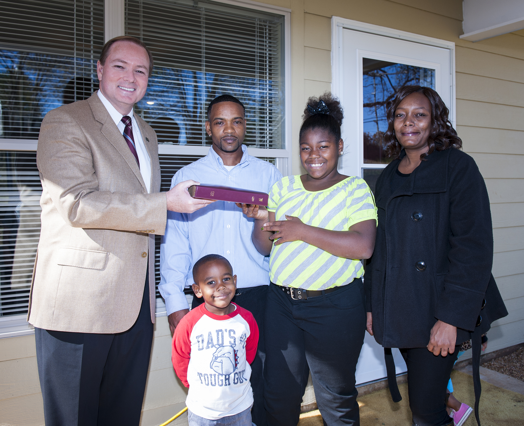 MSU President Mark E. Keenum presents a homeowner's Bible to Marcus, Zoe, Raven, and "little" Marcus Hendrix at the Maroon Edition Habitat for Humanity dedication Monday.