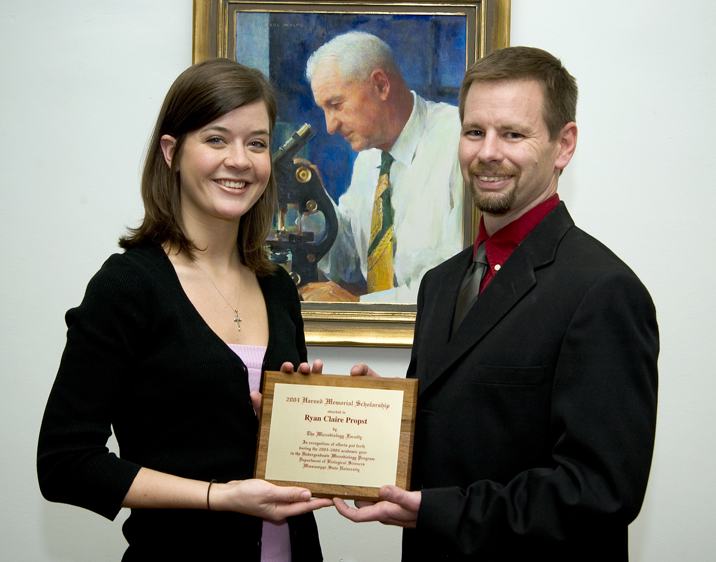 MSU Harned Scholar Ryan Propst and biological sciences faculty member Jeff Echols stand before a portrait of the award's namesake. 